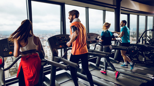 Four people running on treadmils, facing a window